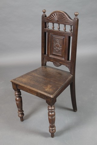 A Victorian oak hall chair with carved armorial decoration to the back, having a solid seat and raised on turned supports 