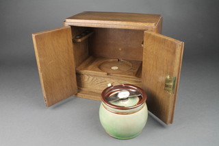 Alfred Dunhill, an Art Deco oak smoker's cabinet with green glazed Doulton tobacco jar, the base impressed Doulton London 26320, the base fitted a drawer with ivory handle enclosed by a pair of panelled doors, labelled Alfred Dunhill Ltd. The White Spot 11"h x 12"w x 7"d 