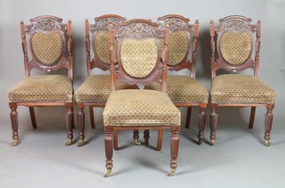 A set of 5 Victorian carved walnut dining chairs with upholstered seats and backs, raised on spiral turned supports, brass caps and casters
