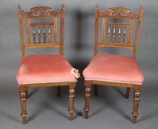 A pair of Edwardian carved walnut stick and rail back dining chairs with bobbin turned decoration, the seats upholstered in pink dralon, raised on turned supports 