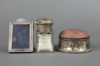 A circular silver pin cushion box, London 1915, a silver mounted toilet bottle and photograph frame