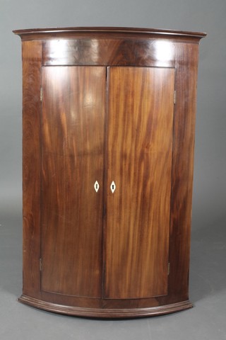 A Georgian mahogany bow front hanging corner cabinet with moulded cornice, the shelved interior enclosed by panelled doors with ivory escutcheons 45 1/2"h x 31"w x 19"d   