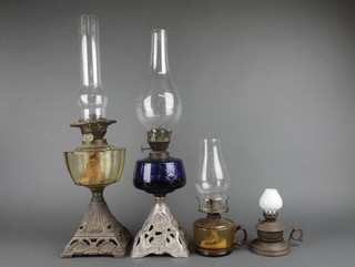 A Victorian clear glass oil lamp reservoir raised on a pierced square tapered iron stand, a ditto blue glass, complete with chimneys together with a glass oil chamber stick and a metal oil chamber stick 