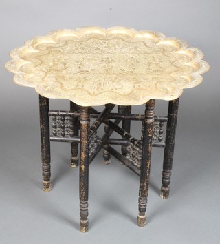 A Benares brass tray with scallop edge, raised on a pierced ebonised folding stand, 22"h x 26 1/2" diam.  