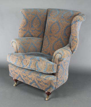 A Victorian style winged tub back armchair upholstered in blue and gold material, raised on turned supports