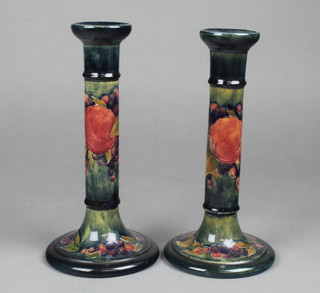 A near pair of Moorcroft candlesticks decorated pomegranate design, signed and impressed 10" and 10 1/4"