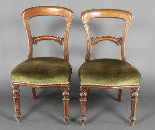 A pair of Victorian walnut balloon back dining chairs with arch shaped mid rails, the seats upholstered in green material, on turned and fluted supports