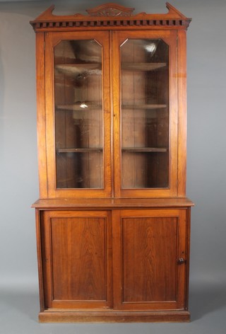 A Victorian mahogany bookcase on cabinet, the upper section fitted a carved and dentil cornice, fitted adjustable shelves enclosed by glazed panelled doors, the base fitted a shelved cupboard enclosed by panelled doors, raised on a platform base 100"h x 49"w x 20"d 