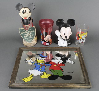 A plastic bar ornament figure of a standing Mickey Mouse 9", a Disney plastic Mickey Mouse money box 6", a Mickey Mouse Donald Duck plate mirror 9" x 11", a glass beaker decorated Minnie Mouse and a plastic beaker decorated Disney figures 