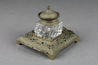 A Victorian gilt metal and brass inkwell, the square cut glass inkwell raised on a pierced brass base  