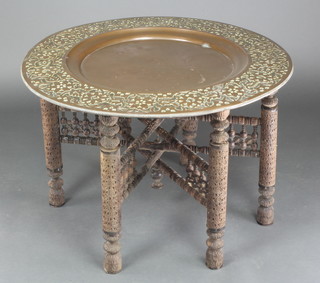 A heavily embossed circular Indian brass tray, raised on a carved hardwood folding stand 21" diam.