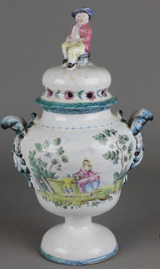 A 19th Century Continental faience baluster vase and cover with seated figural finial and scroll handles, the body decorated with a landscape scene and flowers 11" 