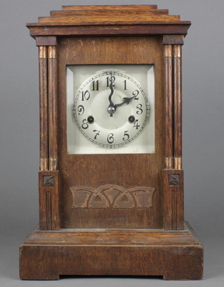 An Art Nouveau 8 day striking mantel clock with square silvered dial and Arabic numerals contained in an oak case with columns to the side 