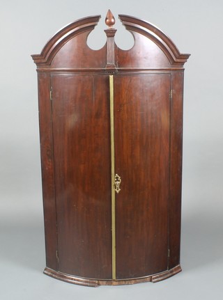 An Edwardian mahogany bow front hanging corner cabinet with broken pediment and shelved interior enclosed by a panelled door with brass bezel 50"h x 29"w x 20"d 