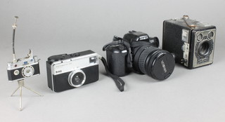 A Minolta Dynax 303 SI camera complete with lens marked AF zoom 28-80mm 1:3.5 (22-56), a Brownie E box camera, a Kodak instamatic 33 camera and a Japanese K.K.W lighter in the form of a camera and tripod 