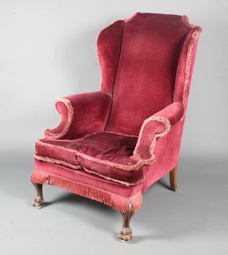 A Georgian style winged armchair upholstered in red material, raised on carved paw feet 