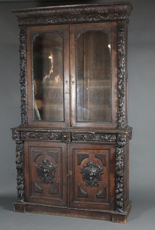 A Victorian carved oak bookcase on cabinet, the upper section with carved moulded cornice, the shelved interior enclosed by glazed panelled doors, the base fitted 2 long drawers above a double cupboard, heavily carved throughout 95"h x 56"w x 14 1/2"d 