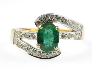 An 18ct yellow gold emerald and diamond cross-over ring, the oval centre stone approx. 1ct surrounded by brilliant cut diamonds approx. 0.35ct, size O
