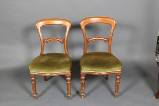 A pair of Victorian walnut balloon back dining chairs with arch shaped mid rails, the seats upholstered in green material, on turned and fluted supports 