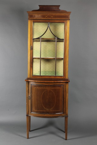 An Edwardian inlaid mahogany display cabinet with crossbanded top, the upper section fitted adjustable shelves enclosed by astragal glazed panelled doors, the bow front base fitted a cupboard enclosed by a panelled door, raised on square tapered supports 77 1/2"h x  25"w x 14"d 