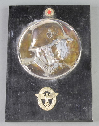 A silvered profile plaque of a soldier decorated 2 cap badges and raised on an ebony base 