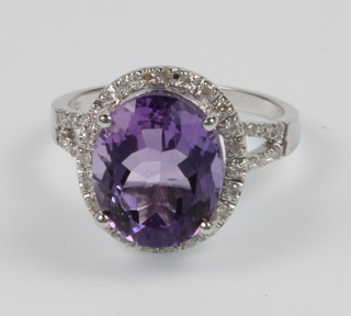 A 14ct white gold diamond and oval amethyst dress ring, the centre stone approx. 5.8ct surrounded by brilliant cut diamonds approx. 0.4ct, size M