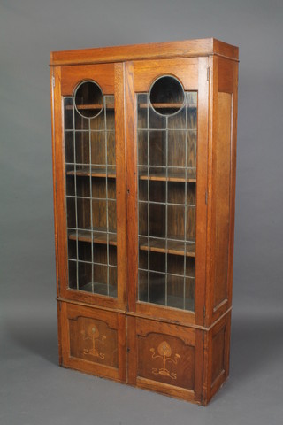 An Art Nouveau oak bookcase, fitted adjustable shelves enclosed by lead glazed panelled doors, the base fitted a cupboard enclosed by panelled doors 68"h x 35 1/2"w x 13"d  