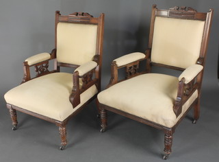 A pair of Victorian carved walnut open arm chairs, the seat back and arms upholstered in cream coloured material, on turned supports  