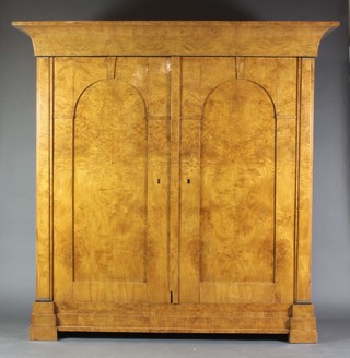 A handsome 19th Century Biedermeier armoire with moulded cornice, the interior fitted hanging space and shelves, enclosed by a pair of arched panelled doors with keystone decoration, raised on a stepped base 69"h x 75"w x 27"d 