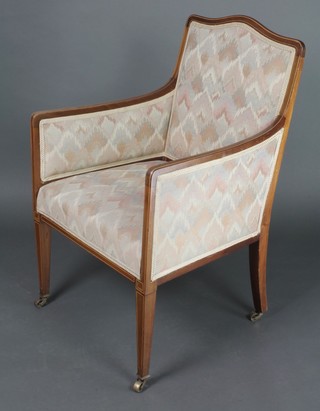 An Edwardian inlaid mahogany show frame armchair with upholstered seat and back ending in brass caps and castors