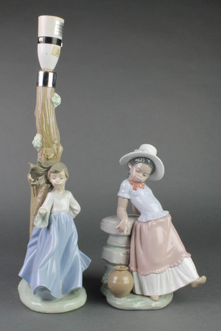 A Lladro figure of a young girl leaning against a wall. 5158 9" and a Nao table lamp with a girl standing beside a tree 12" 