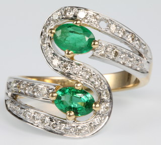 An 18ct yellow gold emerald and diamond cross-over open ring, the 2 oval cut emeralds approx. 1.24ct surrounded by brilliant cut diamonds approx. 0.67ct, size O