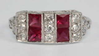 An 18ct white gold and ruby Art Deco style dress ring, the 4 Princess cut rubies surrounded by 15 cut brilliant diamonds, size L 1/2