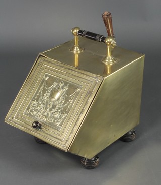 A brass wedge shaped coal bin with embossed hinged lid, complete with shovel, raised on bun feet 