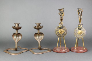 A pair of bronze candlesticks decorated military trophies, the sconces in the form of helmets 12"h (1 sconce has been soldered) together with a pair of brass candlesticks in the form of cobras 7" 