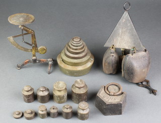 A triangular iron house bell hung 3 cow bells, a set of 8 graduated brass weights, a small balance and a collection of various weights 