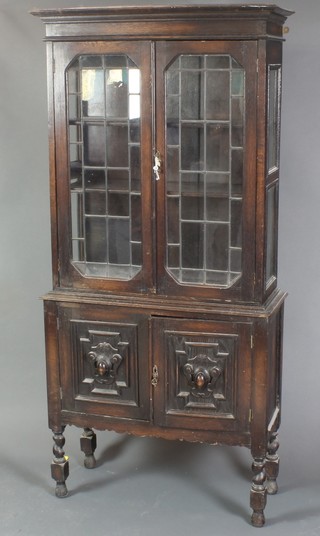 A carved oak display cabinet, the upper section with moulded cornice, the interior fitted shelves enclosed by lead glazed panelled doors, the base fitted a double cupboard enclosed by panelled doors on turned supports 63"h x 30"w x 11 1/2"d