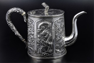 An early 20th Century Chinese silver repousse oval tea pot with panels of flowers, dragons, bamboo and carp, with an armorial panel and ivory resistors, 466g