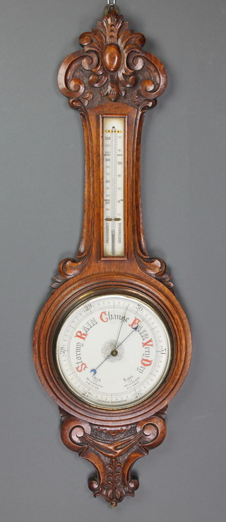 An aneroid barometer and thermometer with enamelled dial, contained in a carved oak wheel case 
