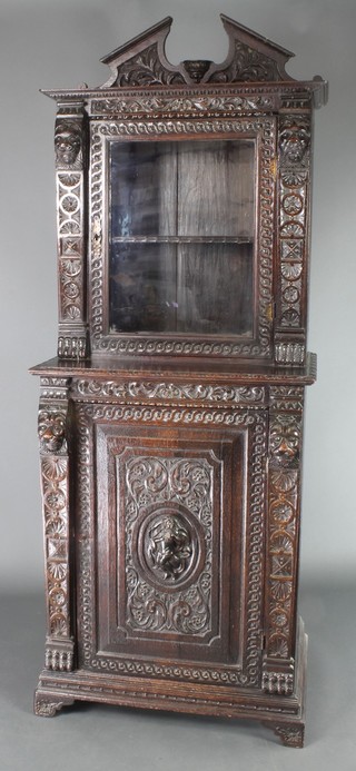 A Victorian carved and ebonised oak cabinet on cabinet, the upper section with broken pediment, the interior fitted a shelf enclosed by a glazed panelled door, the base fitted a cupboard enclosed by a panelled door, raised on bracket feet 78"h x 28"w x 19"d 