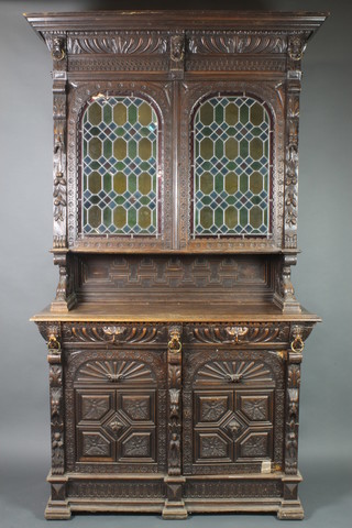 A Victorian carved oak cabinet on cabinet with moulded cornice, heavily carved throughout with lion masks, the upper section fitted shelves enclosed by a pair of arched lead glazed coloured glass panelled doors above a recess, the base fitted 2 long drawers above 2 arched panelled doors, raised on a platform base 101"h x 56"w x 20"d 
