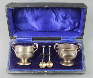 A cased pair of Edwardian silver salts in the form of 2 handled cups with spoons, Chester 1911, 68 grams