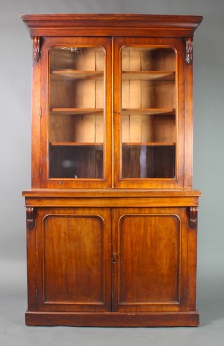 A Victorian mahogany bookcase on cabinet the upper section with moulded cornice, the interior fitted adjustable shelves enclosed by arch shaped glazed panelled doors, the base fitted a cupboard enclosed by a pair of arch panelled doors and having vitruvian scrolls to the sides, 85"h x 50"w x 13"d 