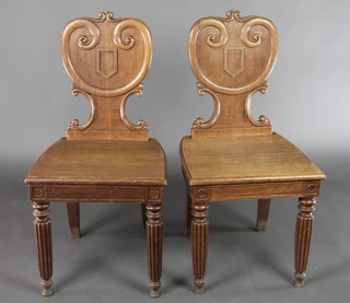 A pair of Victorian carved light oak hall chairs with shield shaped backs and solid seats, raised on turned and reeded supports 