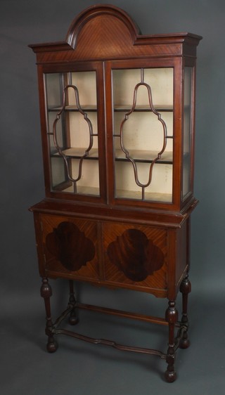An Edwardian Queen Anne style mahogany display cabinet with arched and moulded cornice, the upper section enclosed by astragal glazed panelled doors, the base fitted a cupboard enclosed by shaped and inlaid doors, raised on turned supports with wavy stretcher 78"h x 33 1/2"w x 16"d 