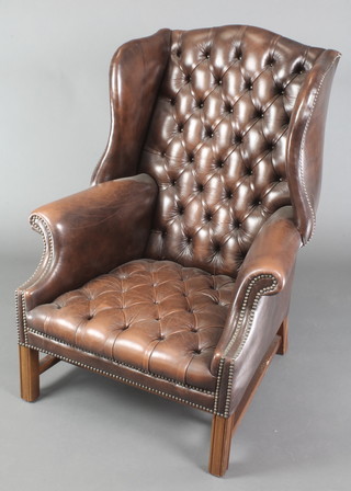 A Georgian style winged armchair upholstered in buttoned back leather, raised on square supports with H framed stretcher 