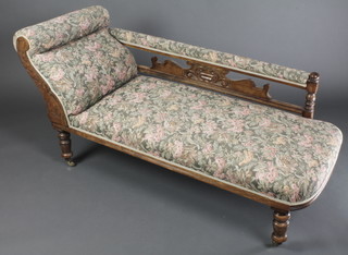 An Edwardian 3 piece carved walnut drawing room suite comprising chaise longue with raised carved back on turned supports and a pair of open arm chairs, all upholstered in floral patterned material 