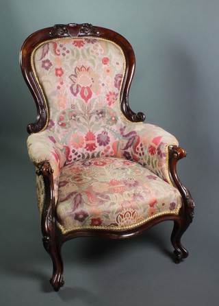 A Victorian carved mahogany show frame armchair upholstered in floral material, the seat of serpentine outline, raised on cabriole supports 