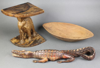 A wedge shaped carved wooden stool supported by a figure of an elephant 13", a carved wooden figure of a crocodile 25" (3 teeth missing) and a boat shaped dish 19" 