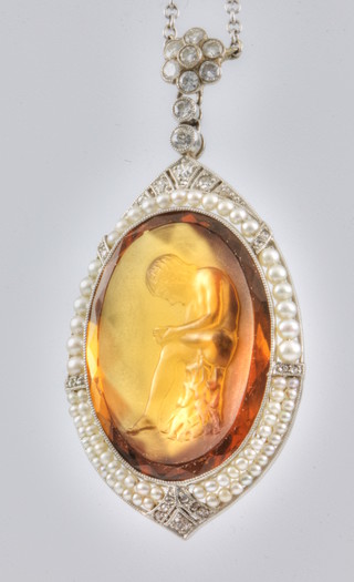 A fine 1920's carved oval citrine pendant depicting Spinario, the white gold mount set with 21 brilliant cut diamonds and 73 seed pearls, 37mm x 22mm, suspended on an 18ct white gold chain set with 9 brilliant cut diamonds and 6 seed pearls, with safety chain 